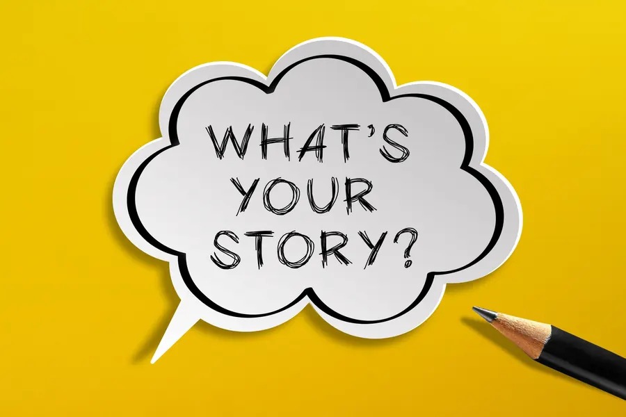 The image shows a bright yellow background with a white, cloud‑shaped speech bubble in the center. Inside the bubble are the black handwritten words “WHAT’S YOUR STORY?”. A black pencil with a light‑brown tip lies in the bottom‑right corner, pointing toward the speech bubble.
