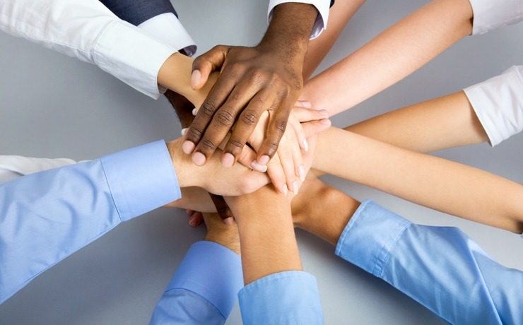 "Multiple hands stacked together in a circle, showing unity and teamwork among diverse people."
