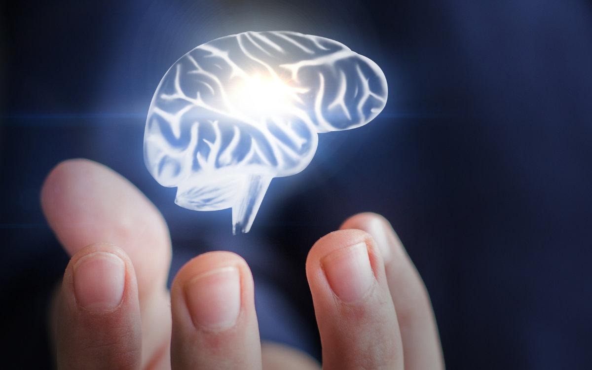 This image shows a futuristic concept of the human brain:

A 3D holographic brain is floating above a person’s fingers, giving a sense of technology and intelligence.

The brain is glowing with white and light blue highlights, emphasizing mental activity, thinking, and cognitive power.

The background is dark blue, which makes the glowing brain stand out more.

The hand under the brain suggests control, focus, or development of mental skills, implying that cognitive ability can be “handled” or “trained.”

The overall visual conveys a modern, tech-inspired idea of enhancing brain power and cognitive abilities.