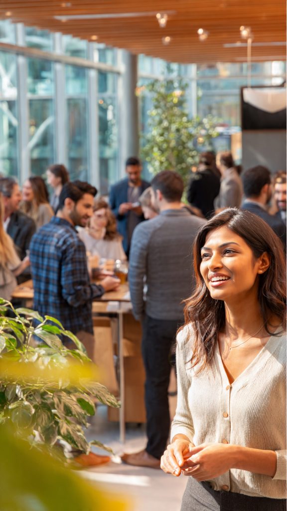 Talent Community
create image A realistic modern office setting where a diverse group of professionals are engaged in a friendly networking conversation. In the foreground, a young South Asian woman in business attire is speaking and smiling while gesturing with her hands. Around her, several colleagues—men and women in smart casual and formal clothing—are listening and interacting in small groups. The environment is bright and spacious with large glass windows, indoor plants, and contemporary furniture. In the background, a screen displays a professional message about building teams, reinforcing a collaborative workplace atmosphere.